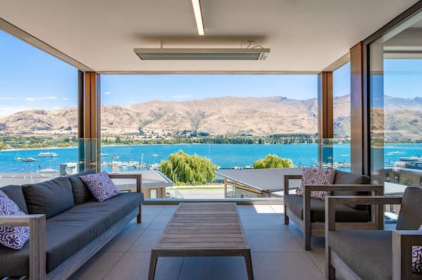 Ein Balkon mit einer Couch, Stühlen und einem Tisch, mit Blick auf einen See und Berge.