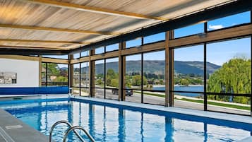 An indoor swimming pool with a view of a lake and mountains.