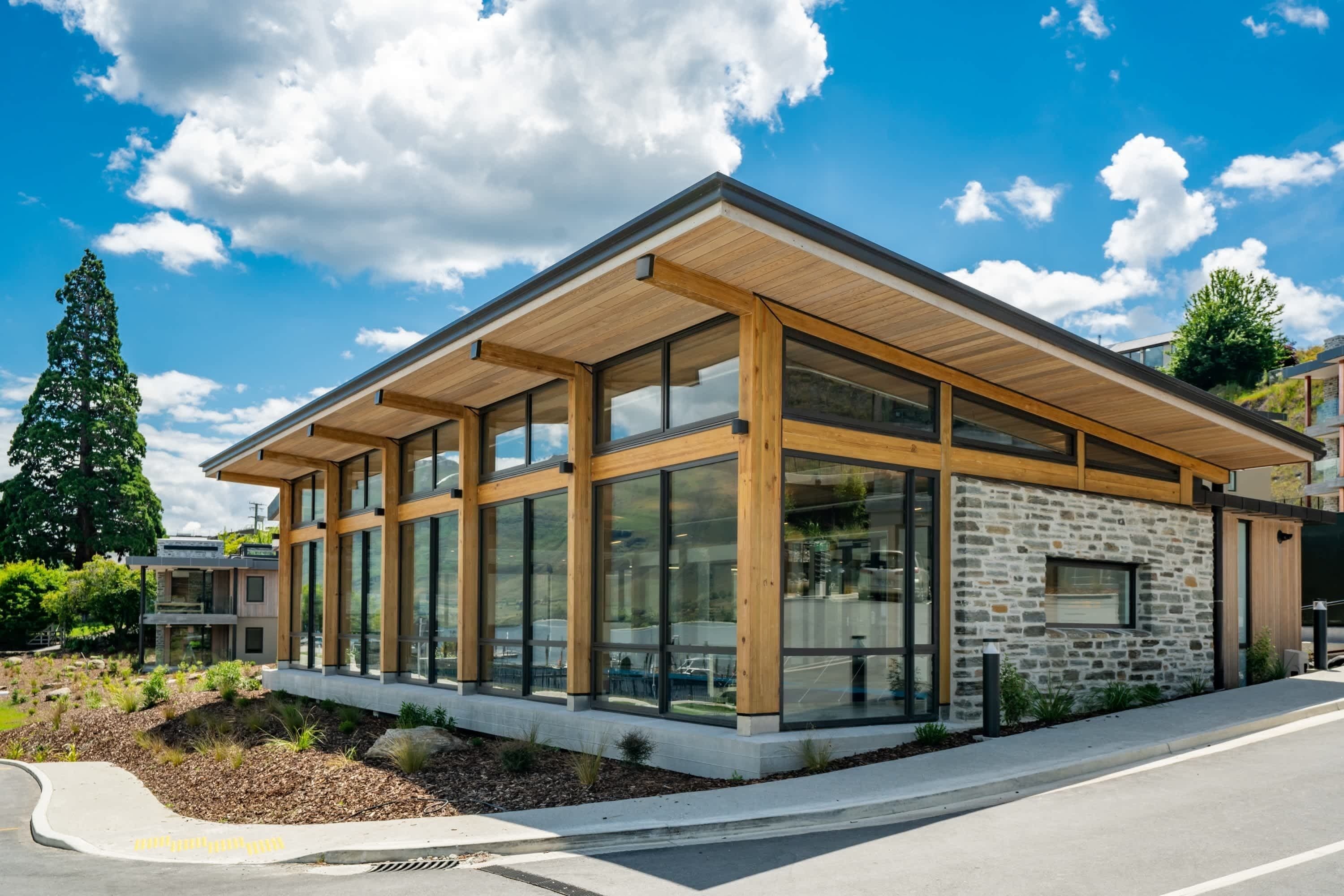 A modern building with large windows, a stone facade, and a wooden roof.