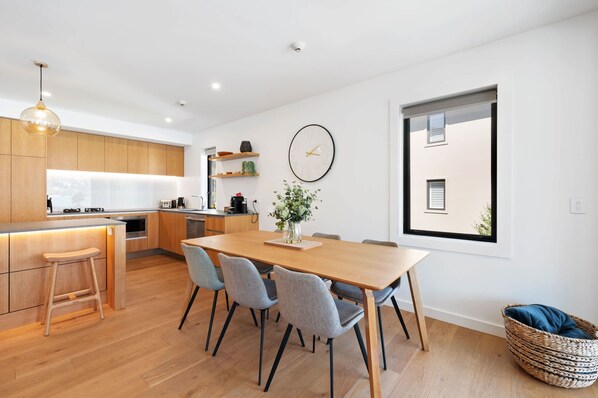 Una cocina moderna con armarios de madera, una mesa de comedor con sillas, un reloj en la pared y un ventanal grande.