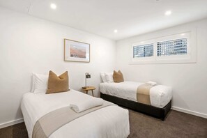 A hotel room with two beds, a small table, a lamp, a framed picture, and a window with blinds. - Lakeside Luxury 2 Bedroom (Wanaka)