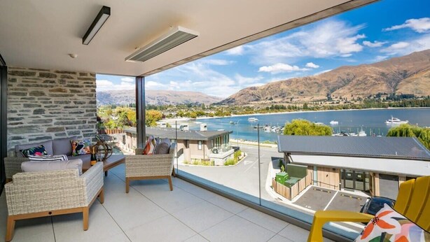 A balcony with wicker furniture, a stone wall, and a view of a lake and mountains. - Luxury Lake View (Wānaka)