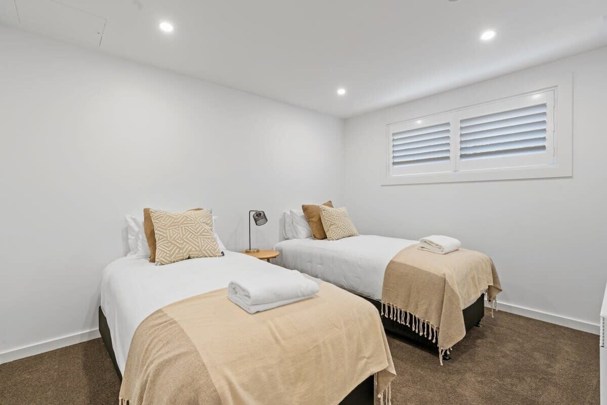 Une chambre avec deux lits, une fenêtre avec des stores, une lampe et une petite table.
