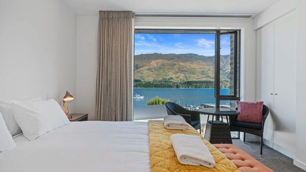 Une chambre d’hôtel avec un lit, un banc avec des serviettes, une table avec des chaises et une vue sur un lac et des montagnes.