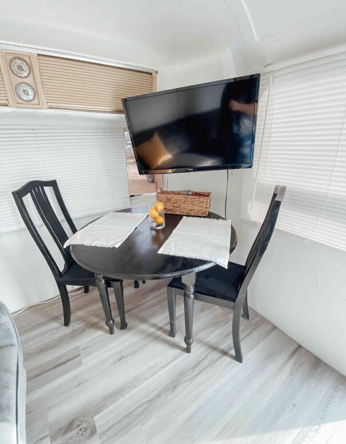 A dining area with a black table, two black chairs, a television on a stand, and a wicker basket on the table.