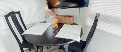 A dining area with a black table, two black chairs, a television on a stand, and a wicker basket on the table.