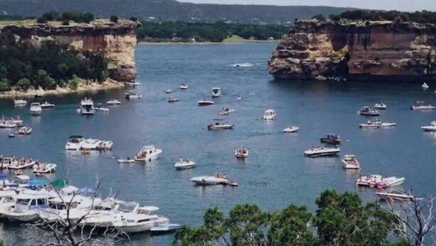 Una zona costera con numerosos barcos atracados y navegando, rodeada de acantilados y vegetación.