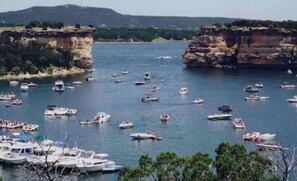 Une zone côtière où de nombreux bateaux sont amarrés et naviguent sur l’eau, le tout étant entouré de falaises et de verdure.