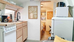 Cocina compacta con estufa, fregadero y microondas. Hay una ventana que proporciona luz natural y una puerta que da a otra habitación.