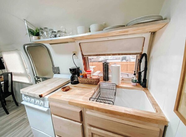 A compact kitchenette with a stove, sink, and wooden countertop.