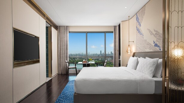 Habitación de hotel con una cama grande, televisión, balcón con vista a la ciudad y un detalle decorativo en la pared.