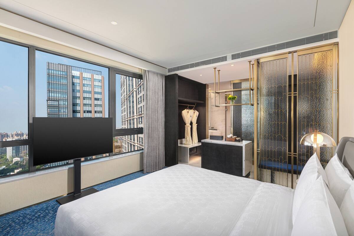 Ein modernes Hotelzimmer mit einem großen Bett, einem Schreibtisch, einem Frisiertisch und Blick auf die Stadt.