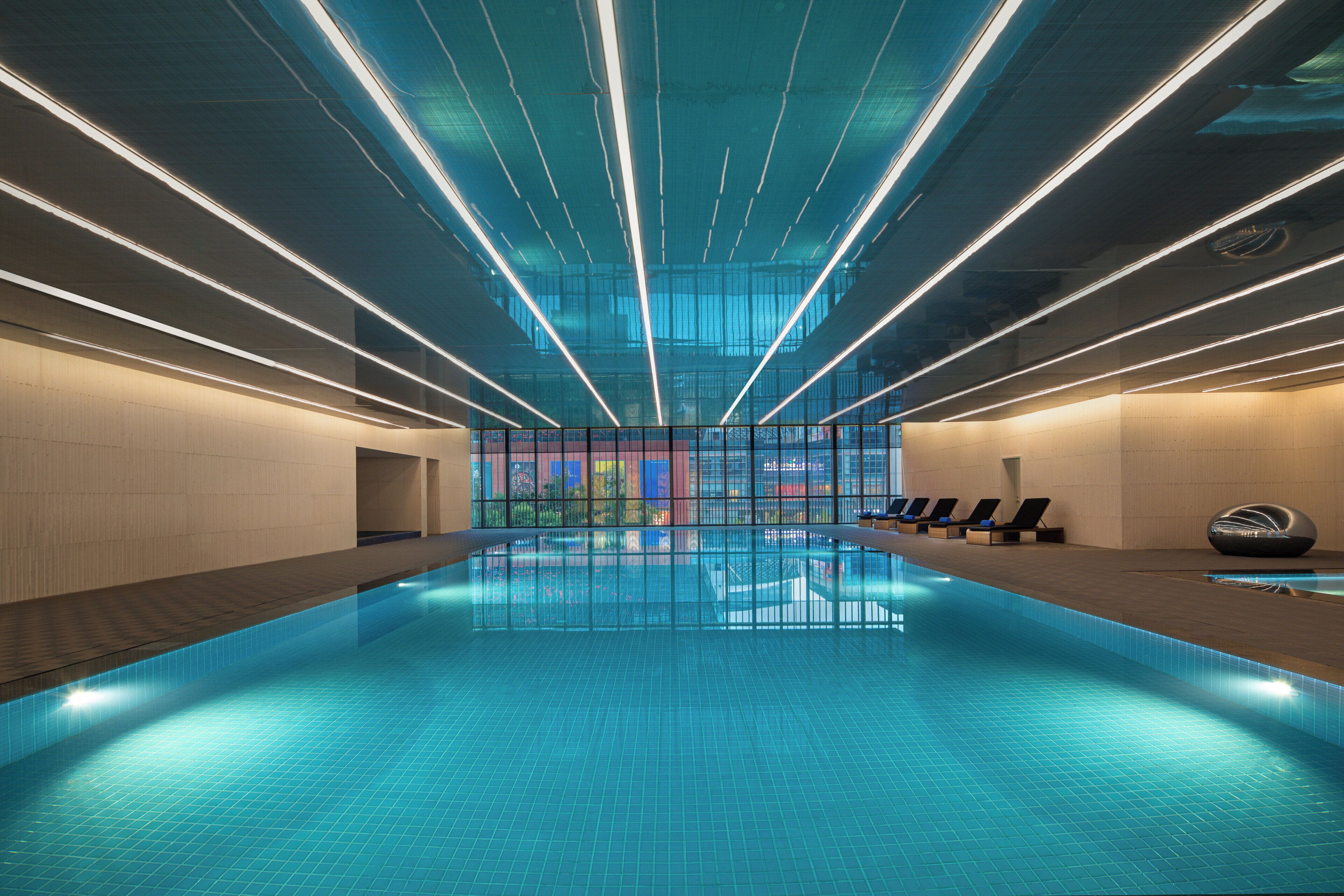 En moderne indendørs swimmingpool med frit udsyn til bybilledet gennem store vinduer.
