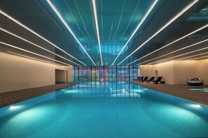 A modern indoor swimming pool with a clear view of the cityscape through large windows. - HUALUXE Shanghai Changfeng Park by IHG (Shanghai)
