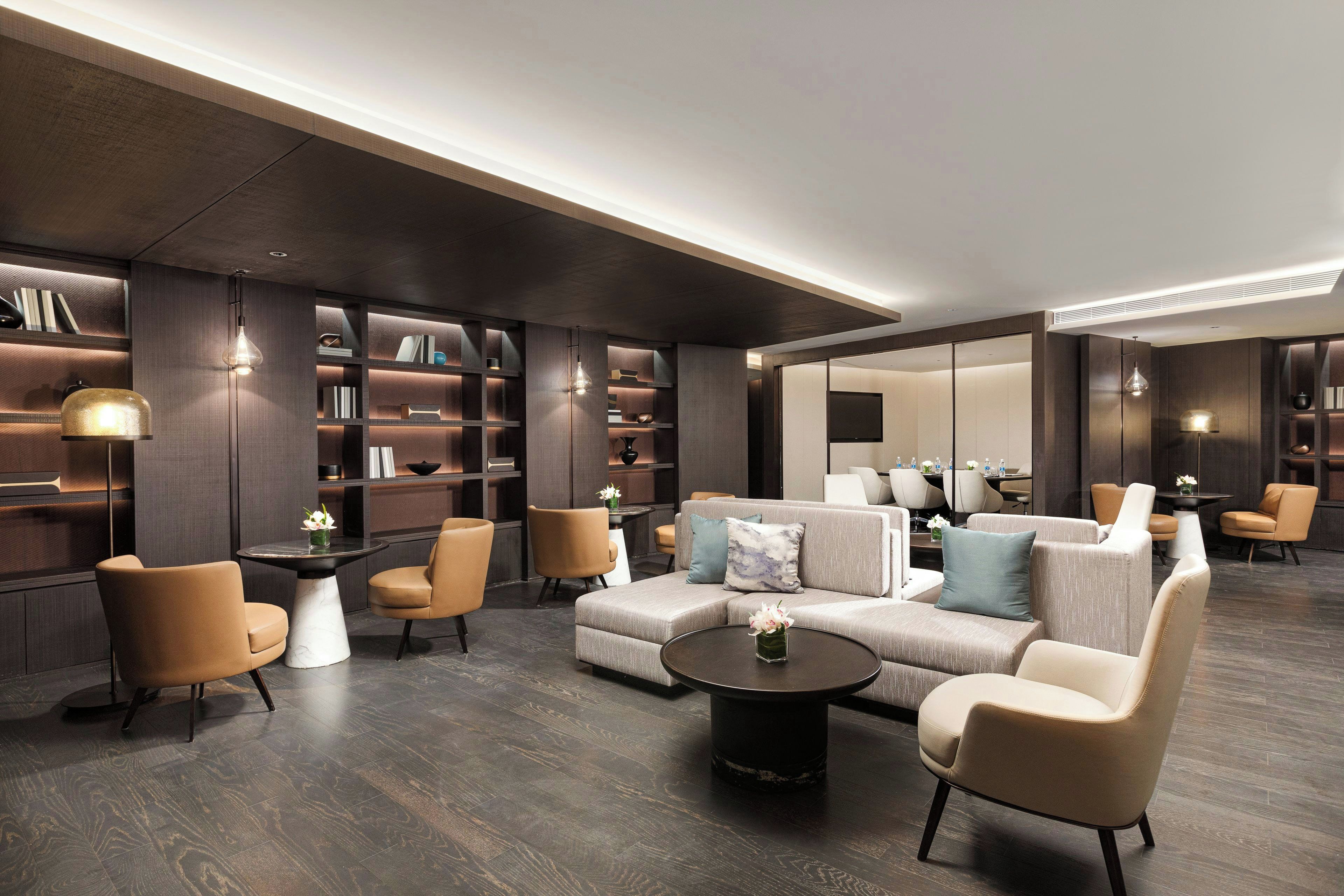 A modern hotel lobby with a sectional sofa, armchairs, a coffee table, and built-in bookshelves.