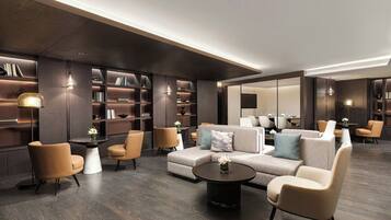 A modern hotel lobby with a sectional sofa, armchairs, a coffee table, and built-in bookshelves.