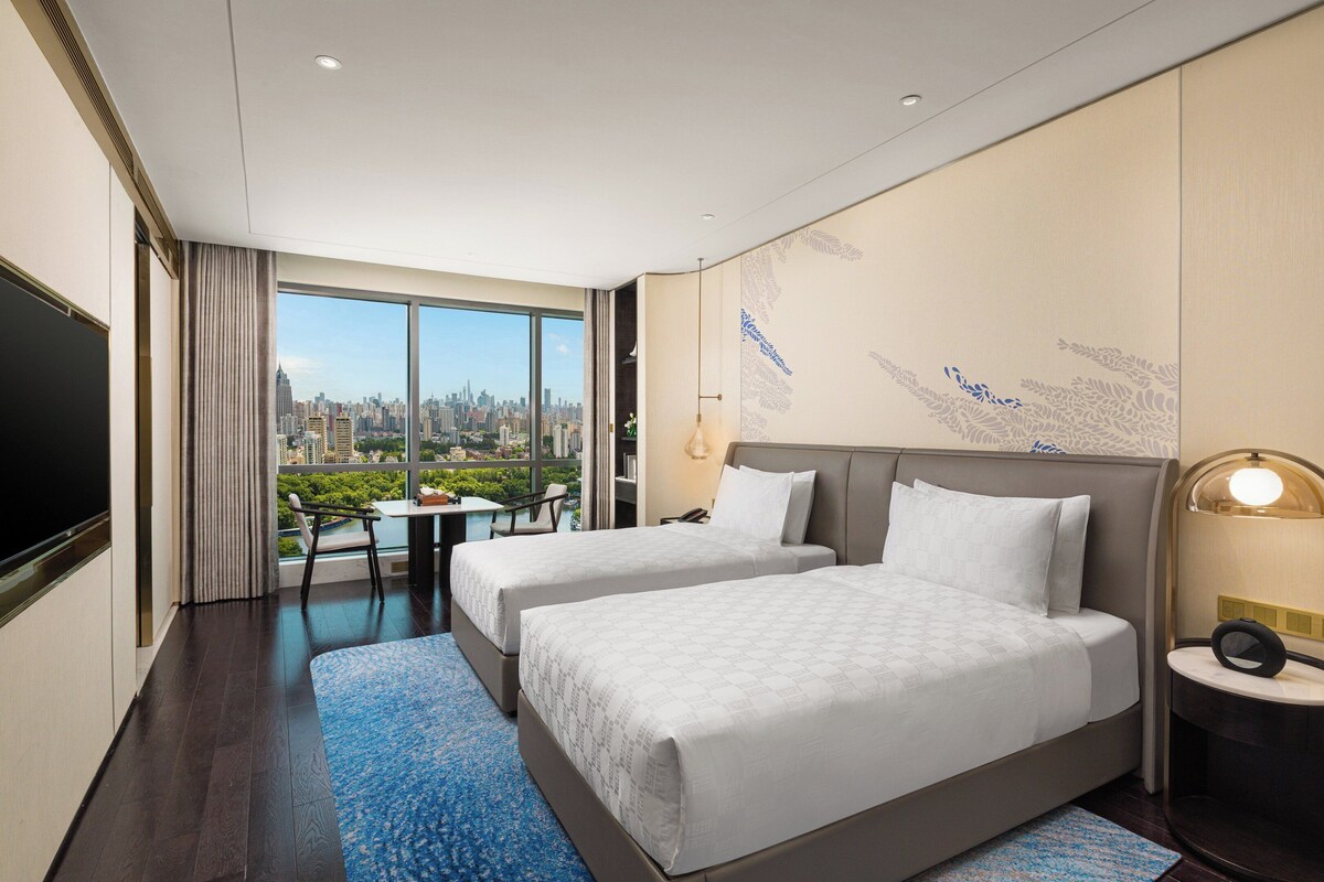 A hotel room with two beds, a city view, a dining area, and a TV.