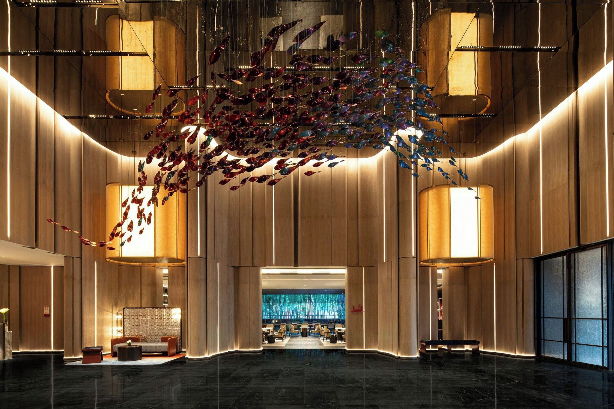 A spacious lobby with a modern design, featuring a central seating area, a large chandelier, and a view into a dining area.