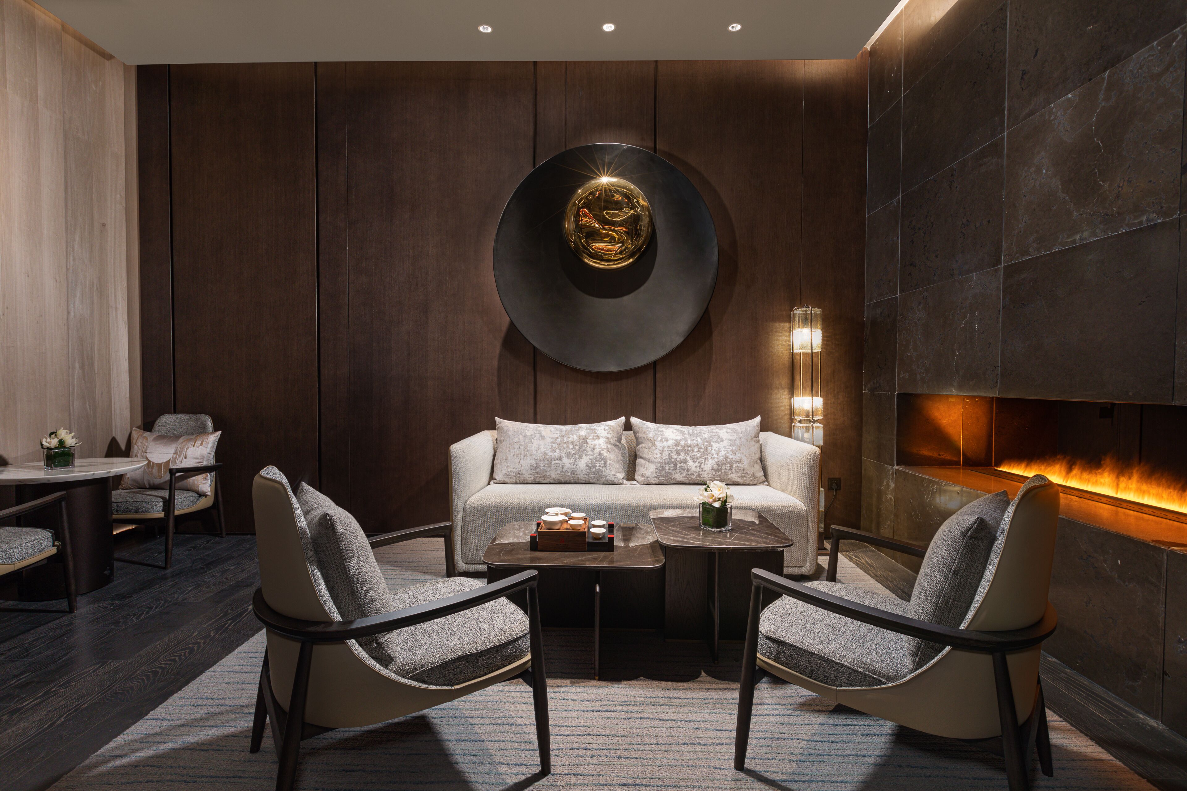 A modern living room with a sofa, two armchairs, a coffee table, and a fireplace.