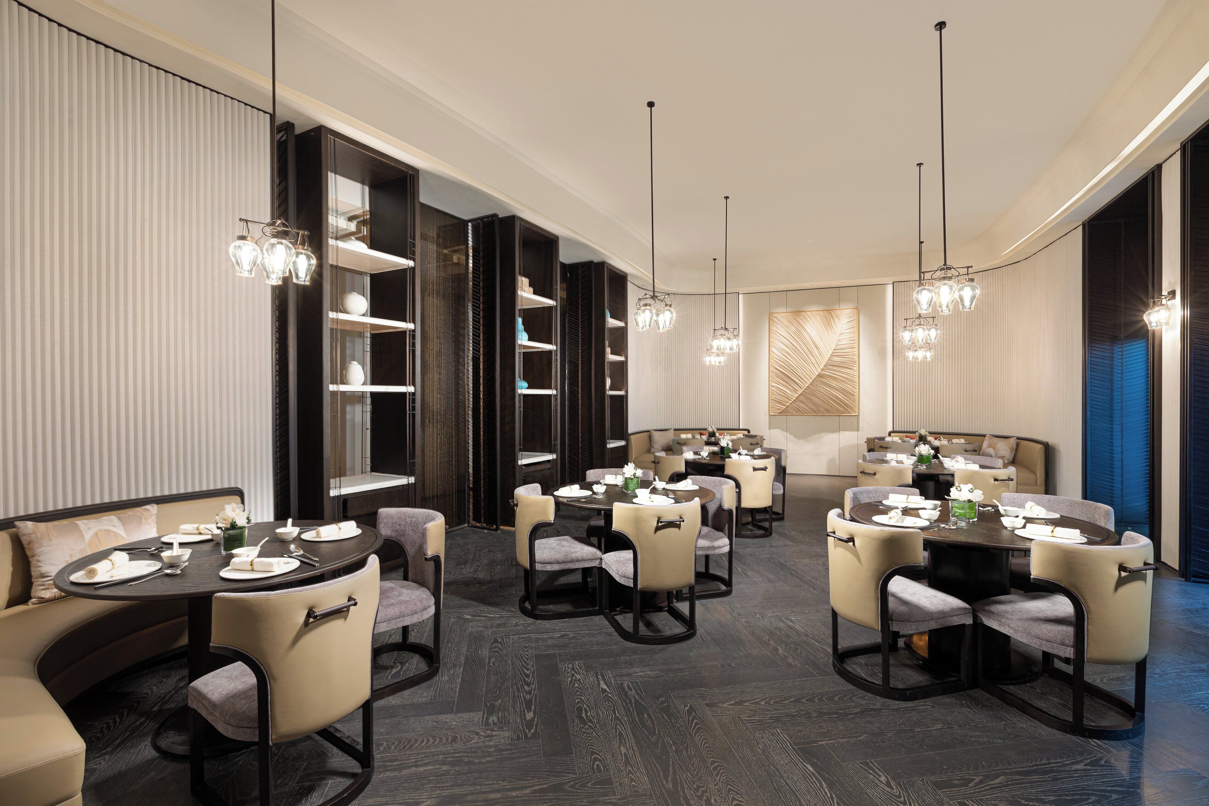 A modern dining area with round tables, cushioned chairs, and pendant lighting.
