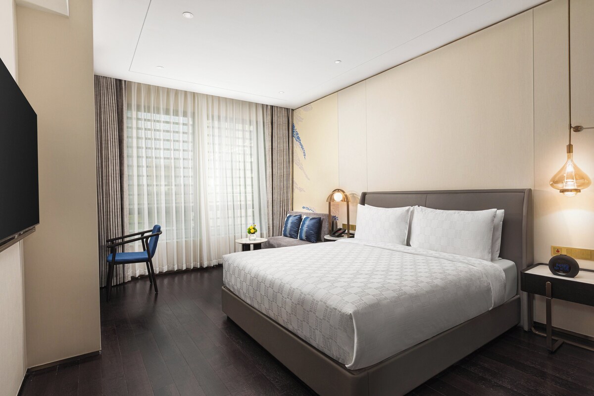 Habitación de hotel con una cama grande, un escritorio, una silla, una mesita con un florero y una lámpara.