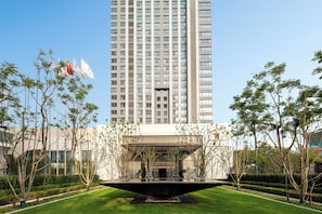 A modern building with a central entrance, surrounded by a well-maintained garden with a water feature in the foreground. - HUALUXE Shanghai Changfeng Park by IHG (Shanghai)