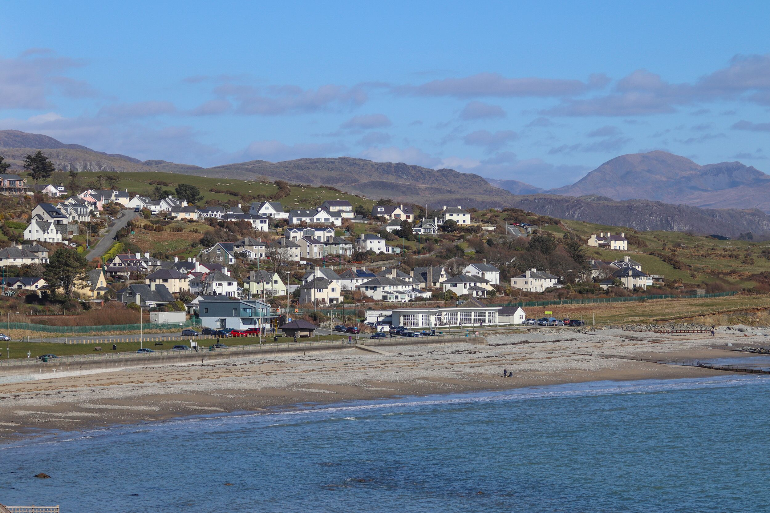 A coastal town with white houses, a beach, and mountains in the background.