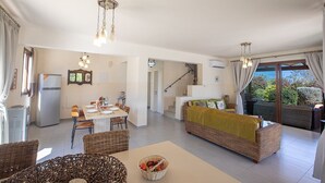 Amplia sala de estar con mesa de comedor, muebles de mimbre y un sofá con una manta verde.