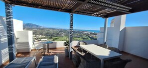 Une terrasse avec une table et des chaises, un pot de fleurs et une vue sur un paysage côtier.