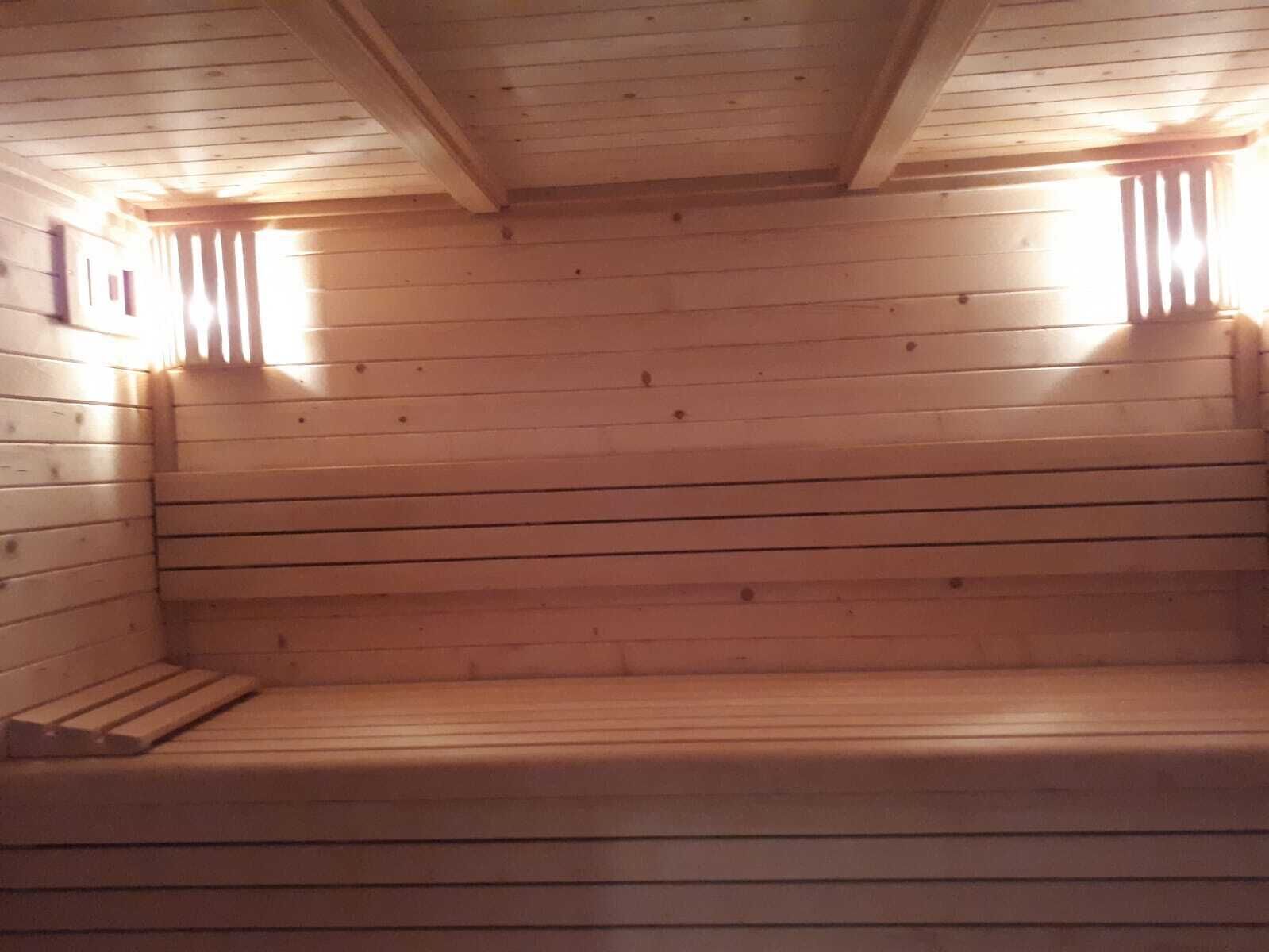 A wooden sauna with benches and two wall-mounted light fixtures.