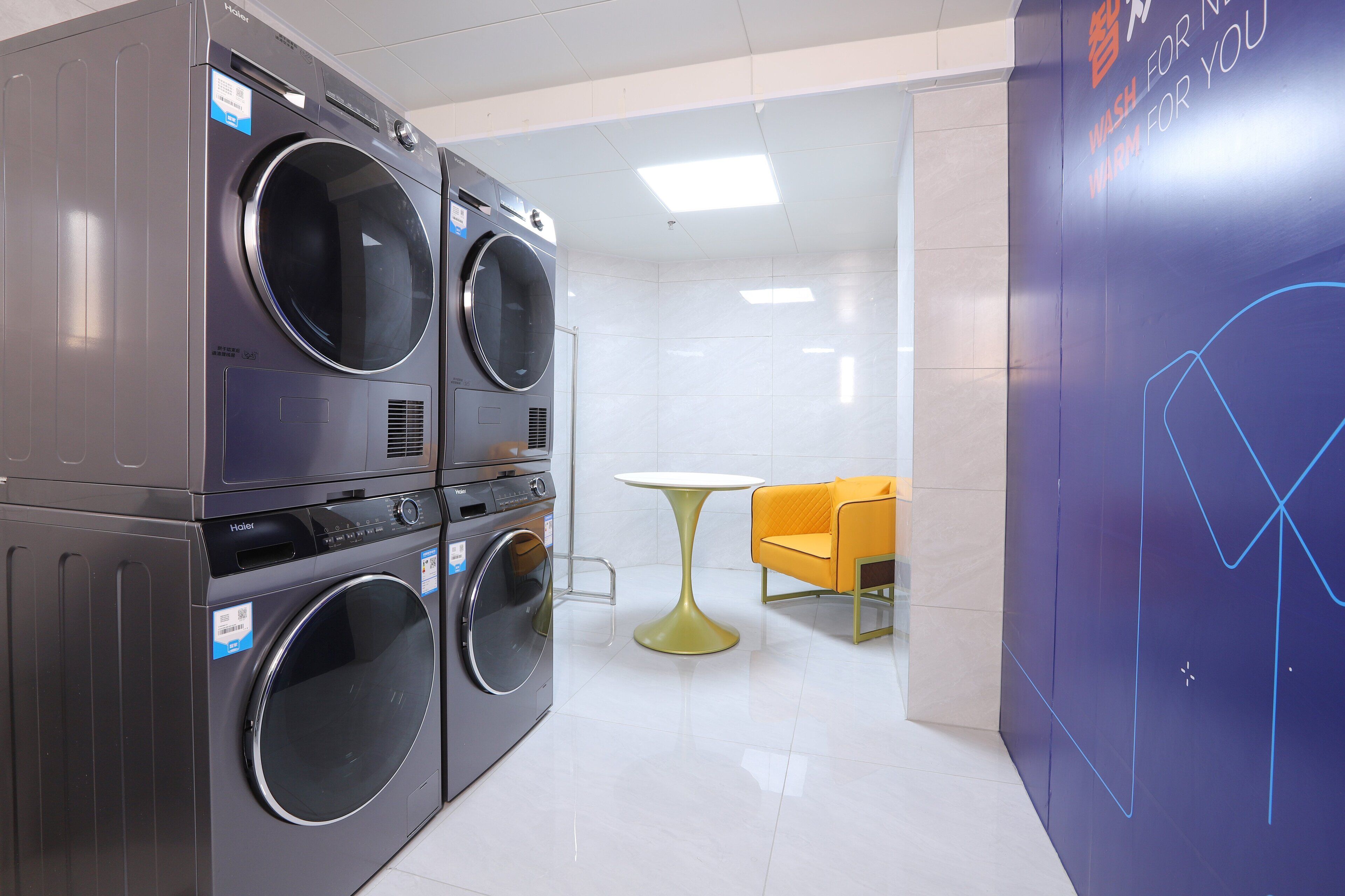 A hotel laundry room with stacked washing machines, a table, and a wall with a graph design.