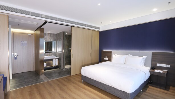Ein modernes Schlafzimmer mit einem großen Bett, einem eingebauten Kleiderschrank, einem Badezimmer mit Spiegel und Holzboden.