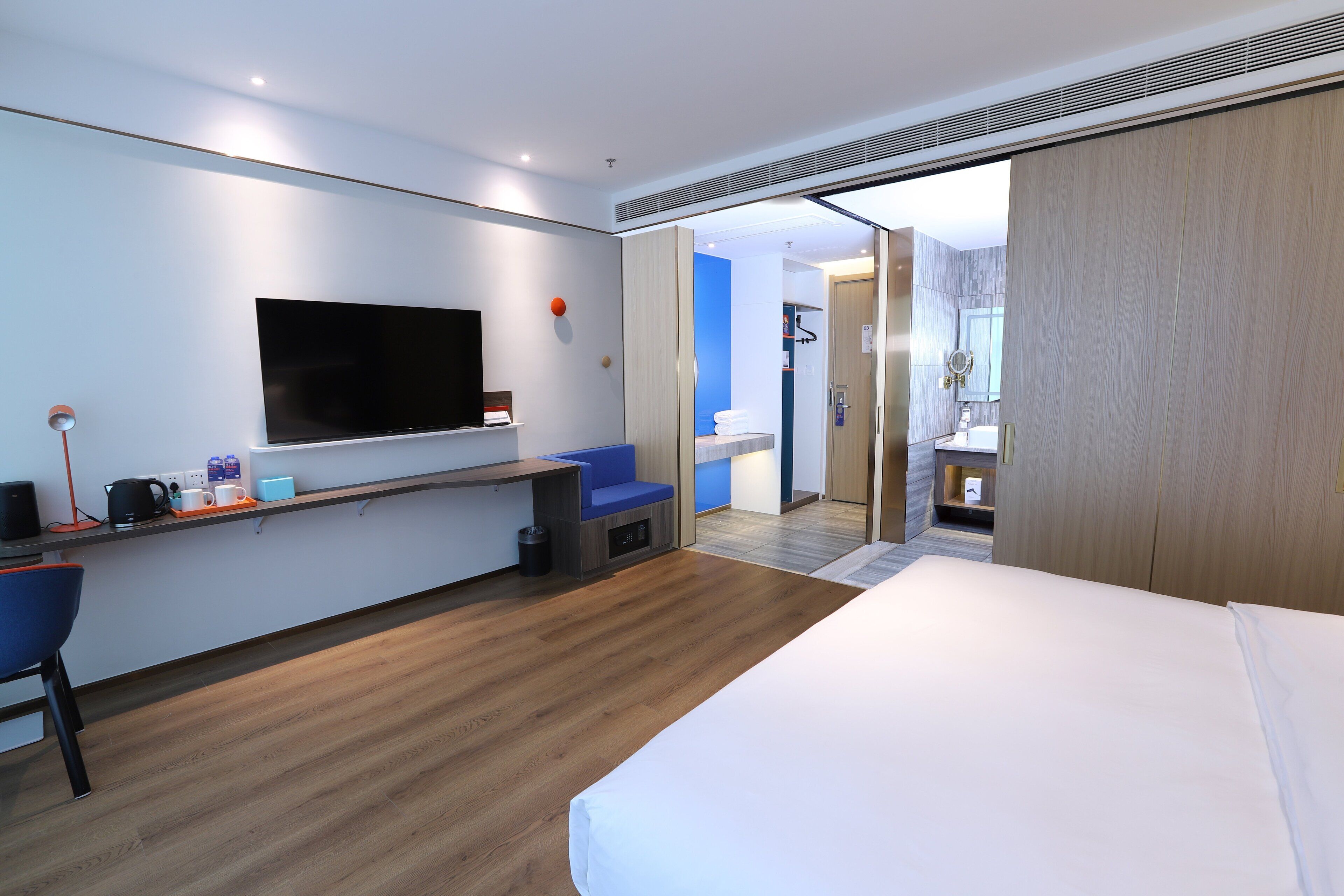 Ein modernes Hotelzimmer mit Bett, Schreibtisch mit Flachbildfernseher, einer Sitzecke und einem durch eine offene Tür einsehbarer Bad.