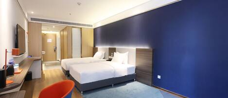 A modern hotel room with a large bed, a desk with a computer, and a chair.