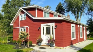 A red single-story house with a white door and windows, a front porch, and two potted plants.