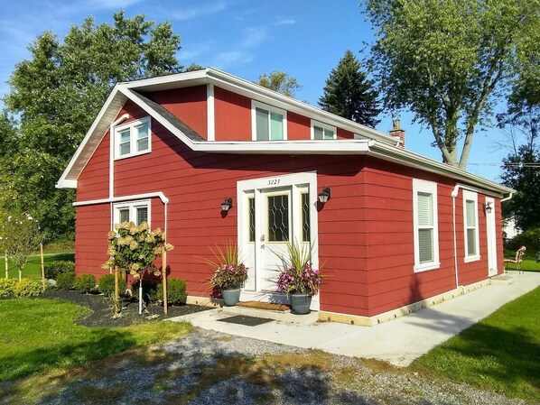 A red single-story house with a white door and windows, a front porch, and two potted plants.