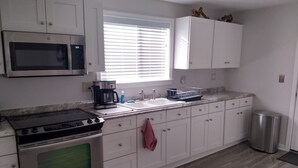 A kitchen with white cabinets, a microwave, a stove, a sink, and a window with blinds.