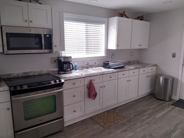 A kitchen with white cabinets, a microwave, a stove, a sink, and a window with blinds.