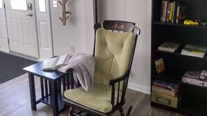 A living room with a rocking chair, a small table with a book, a lamp, and a bookshelf.