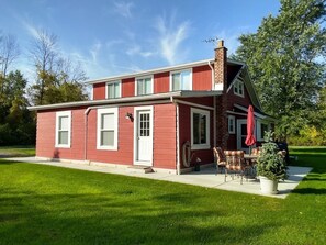 A red two-story house with a front porch, a chimney, and a small patio area with outdoor furniture.