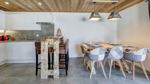 Een moderne keuken met witte kastjes, een houten plafond en een eethoek met een houten tafel en gestreept beklede stoelen.