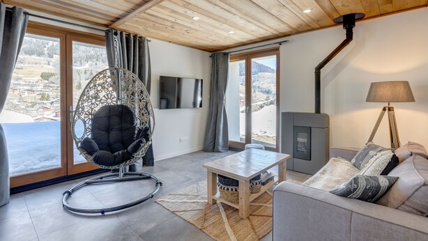 Een moderne woonkamer met een houten plafond, een bank, een hangstoel, een televisie, een open haard en uitzicht op de bergen.