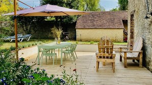 An outdoor patio with a table and chairs, surrounded by a wooden deck and garden.