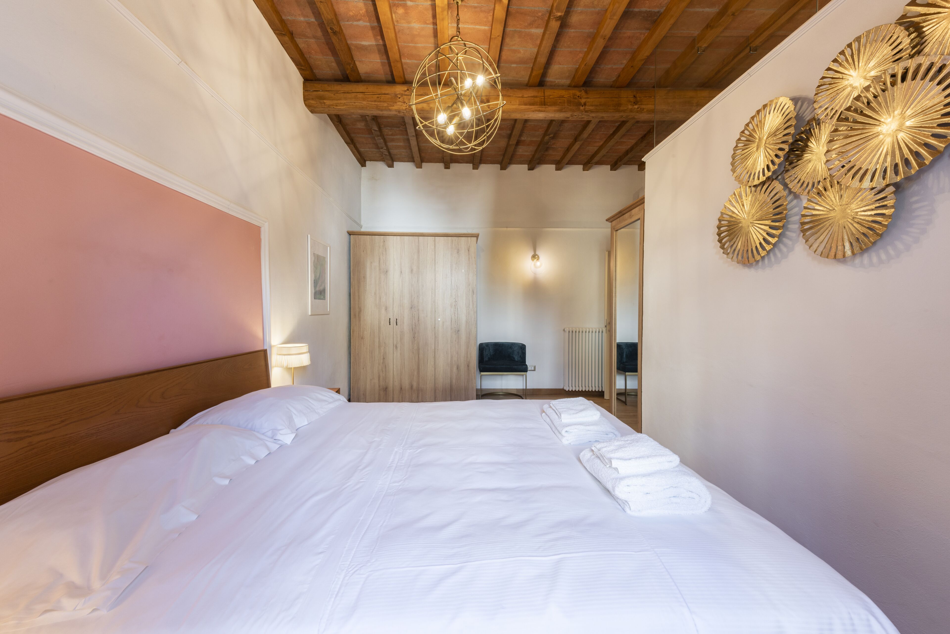 A neatly made bed with white linens and towels, a wooden headboard, a hanging light fixture, and a wall with decorative plates.
