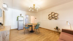 Un salón moderno con una mesa de comedor redonda, sillas color turquesa, un sofá rosa, suelo de madera, un estante hexagonal anclado a la pared con plantas y una lámpara en el techo.