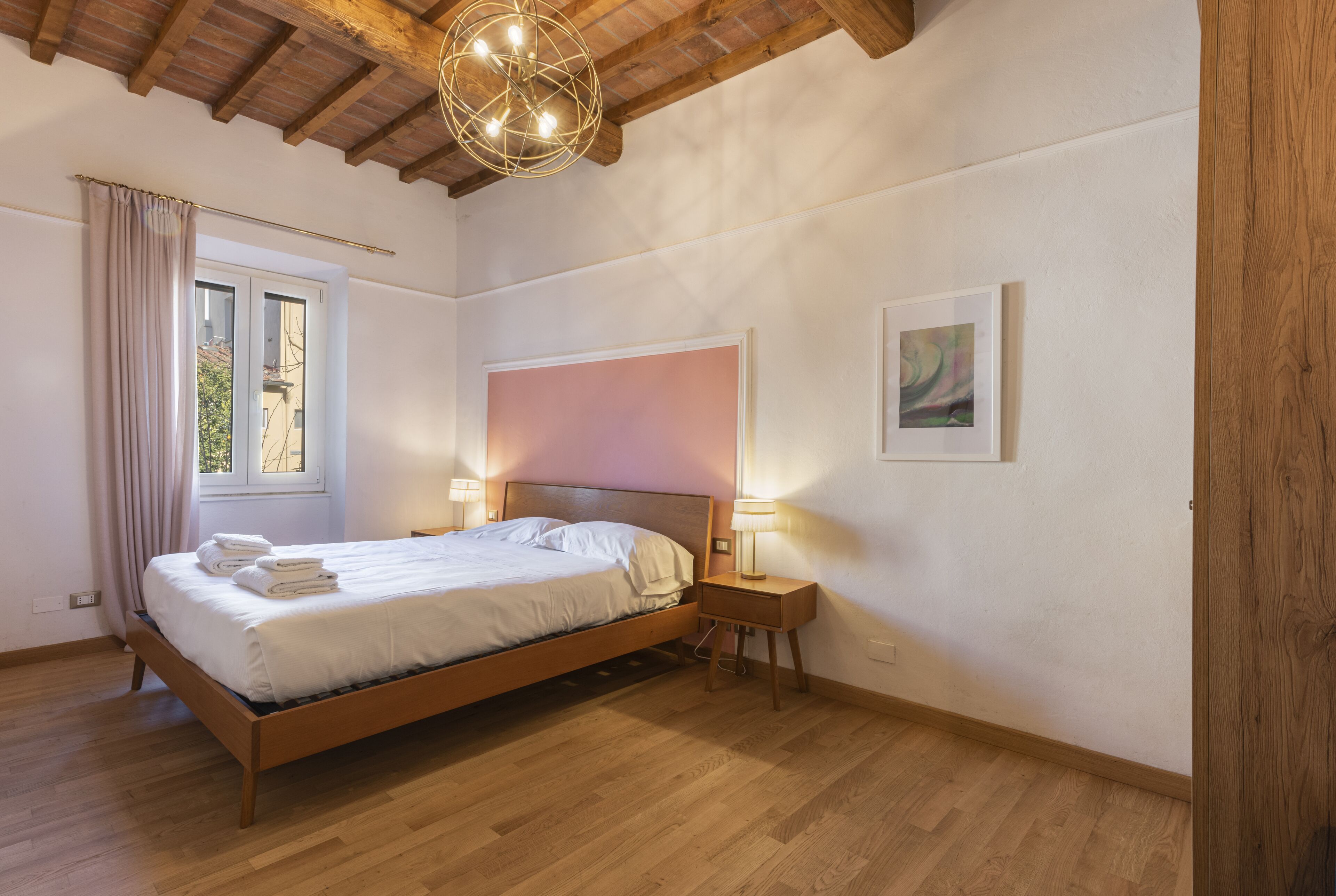 Un dormitorio con una cama de madera, lámparas de noche, una ventana con cortinas e iluminación en el techo.