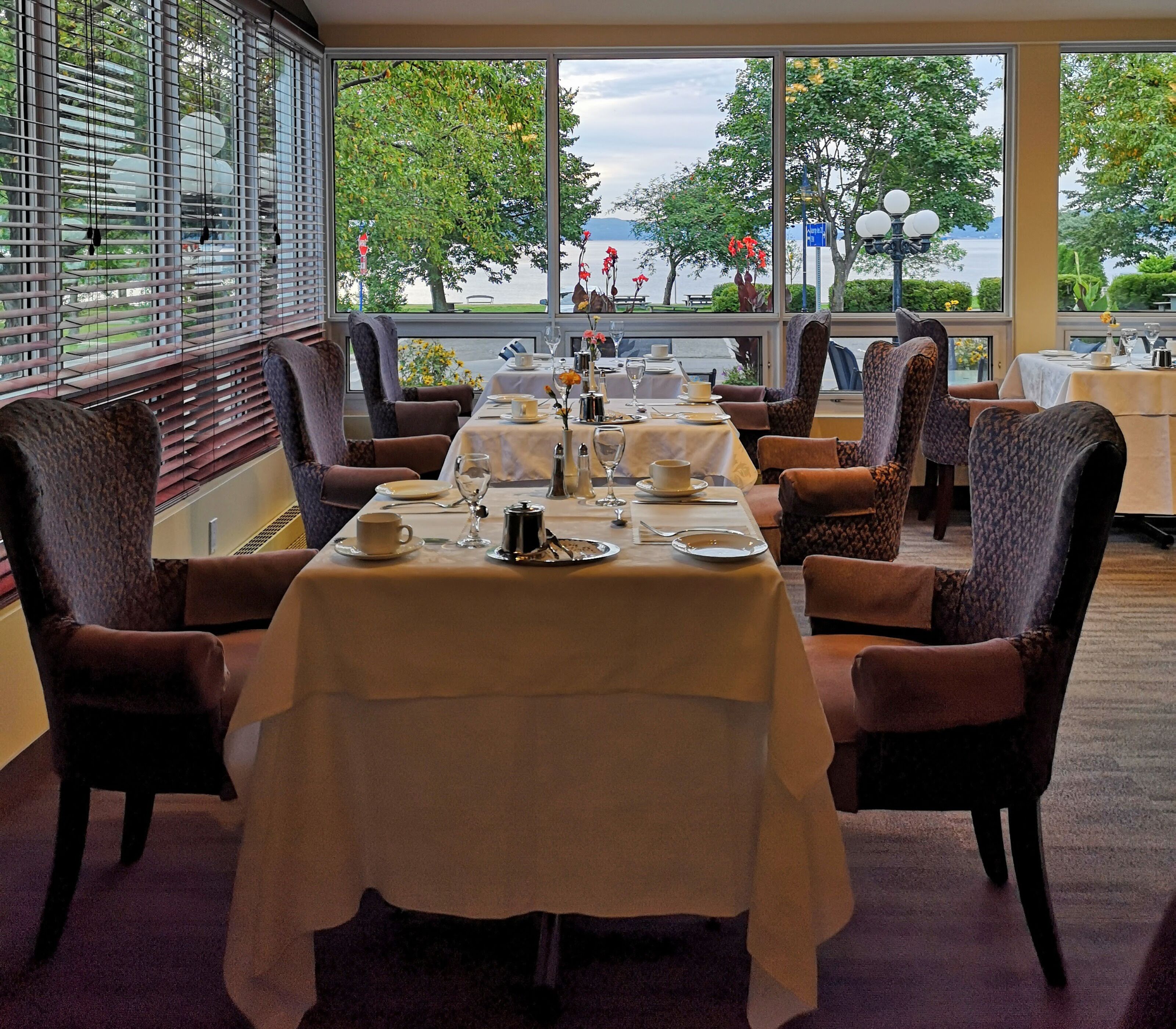 Comedor con mesas dispuestas para una comida, sillas y vistas a un lago a través de amplias ventanas.