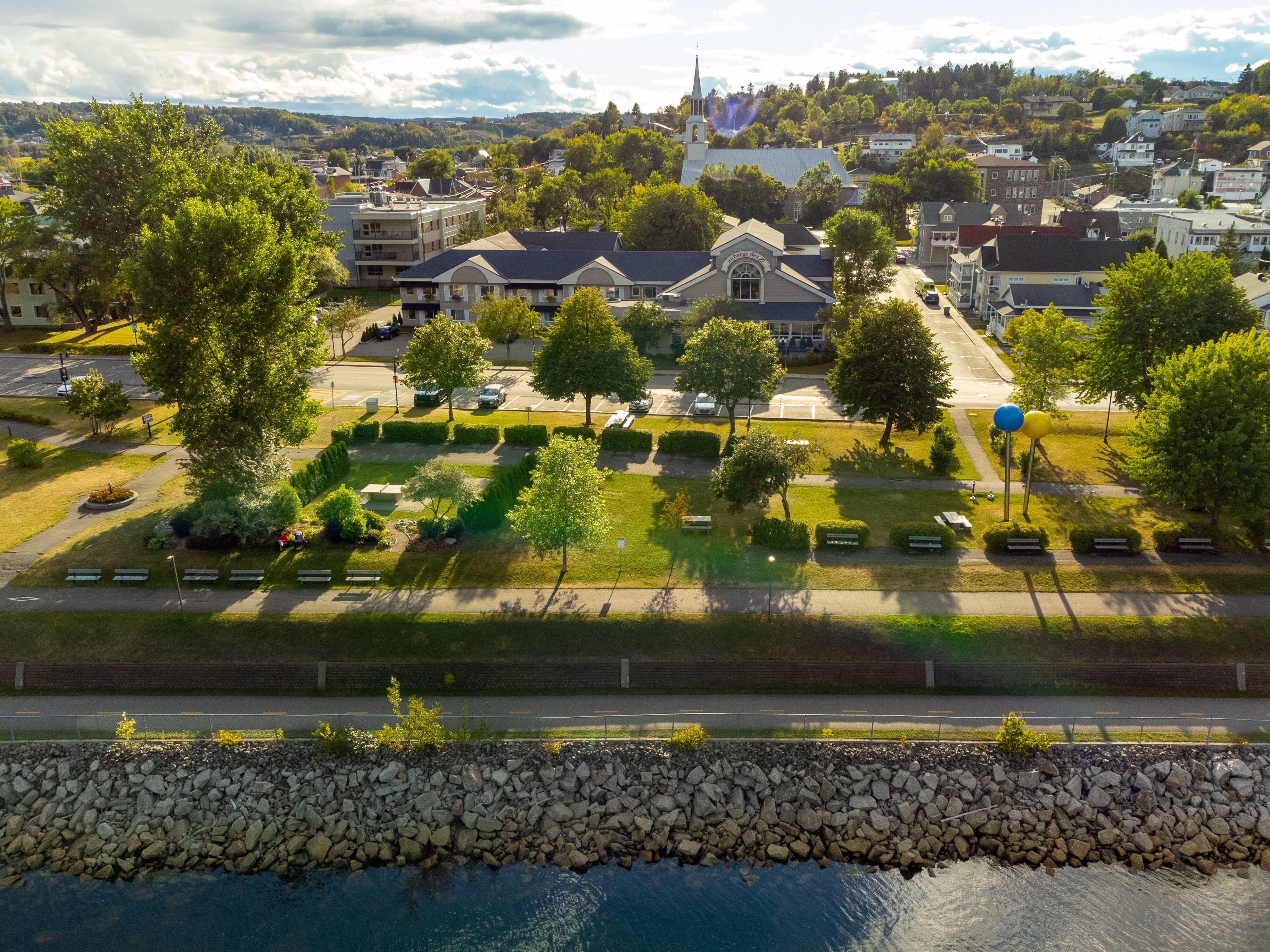 An aerial view of a town with a church, residential buildings, and a park with benches and trees.