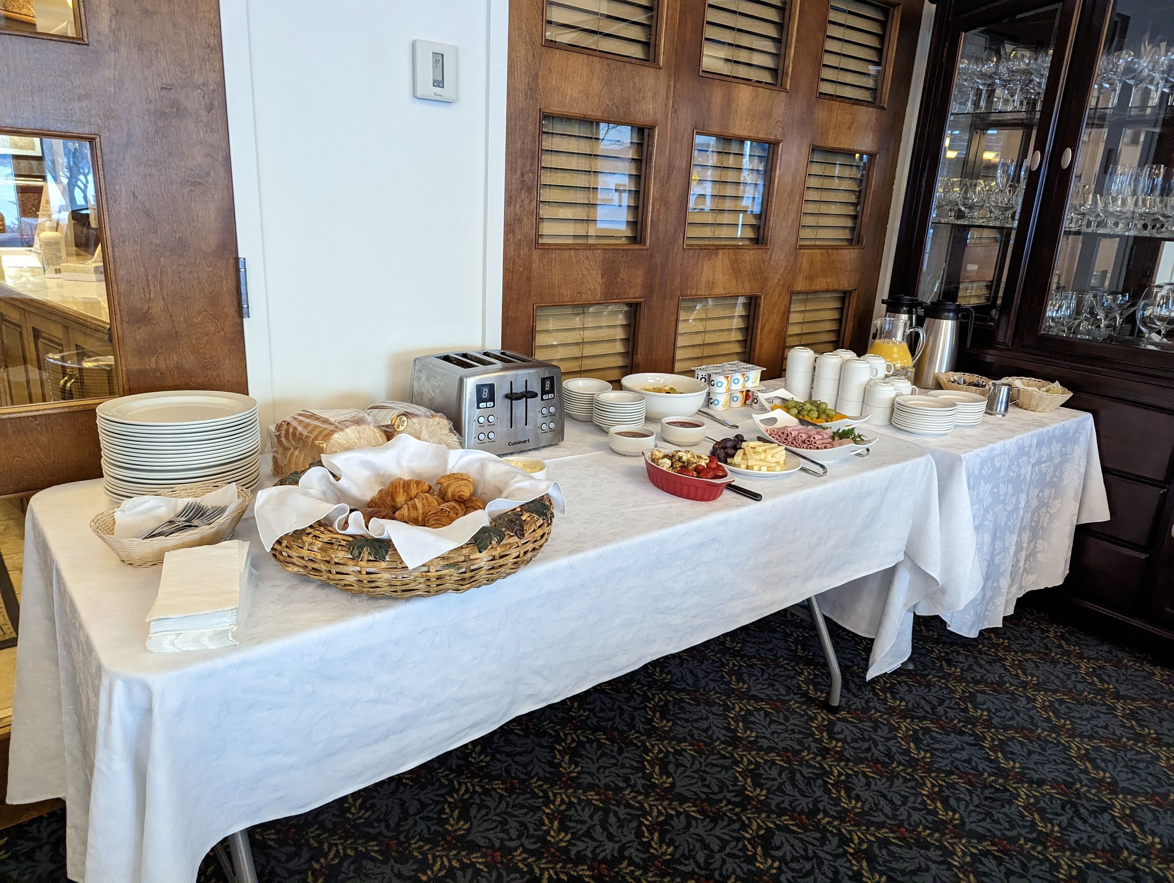 Una mesa de buffet con diversos alimentos y utensilios, un tostador y un termostato en la pared.