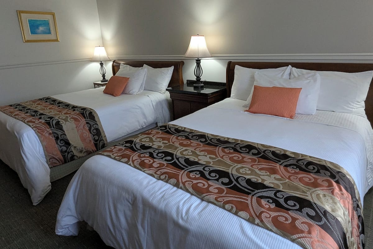Two double beds with white linens, a patterned throw blanket, and a nightstand with a lamp.
